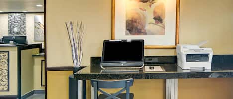 Una mesa de recepción con una computadora portátil, una impresora y un cuadro abstracto enmarcado.