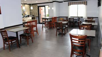 Un restaurante con varias mesas y sillas, una zona de cocina y vistas al exterior.
