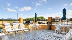 A patio with white plastic chairs and tables, a trash can, and a green umbrella. - Quality Inn DFW Airport North (Irving)