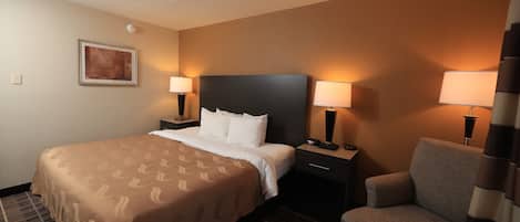 A hotel room with a bed, two bedside lamps, a chair, a nightstand, a wall-mounted picture, and a carpeted floor.