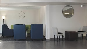 A modern lobby with seating, a wall clock, a round mirror, and recessed ceiling lights. - Quality Inn DFW Airport North (Irving)