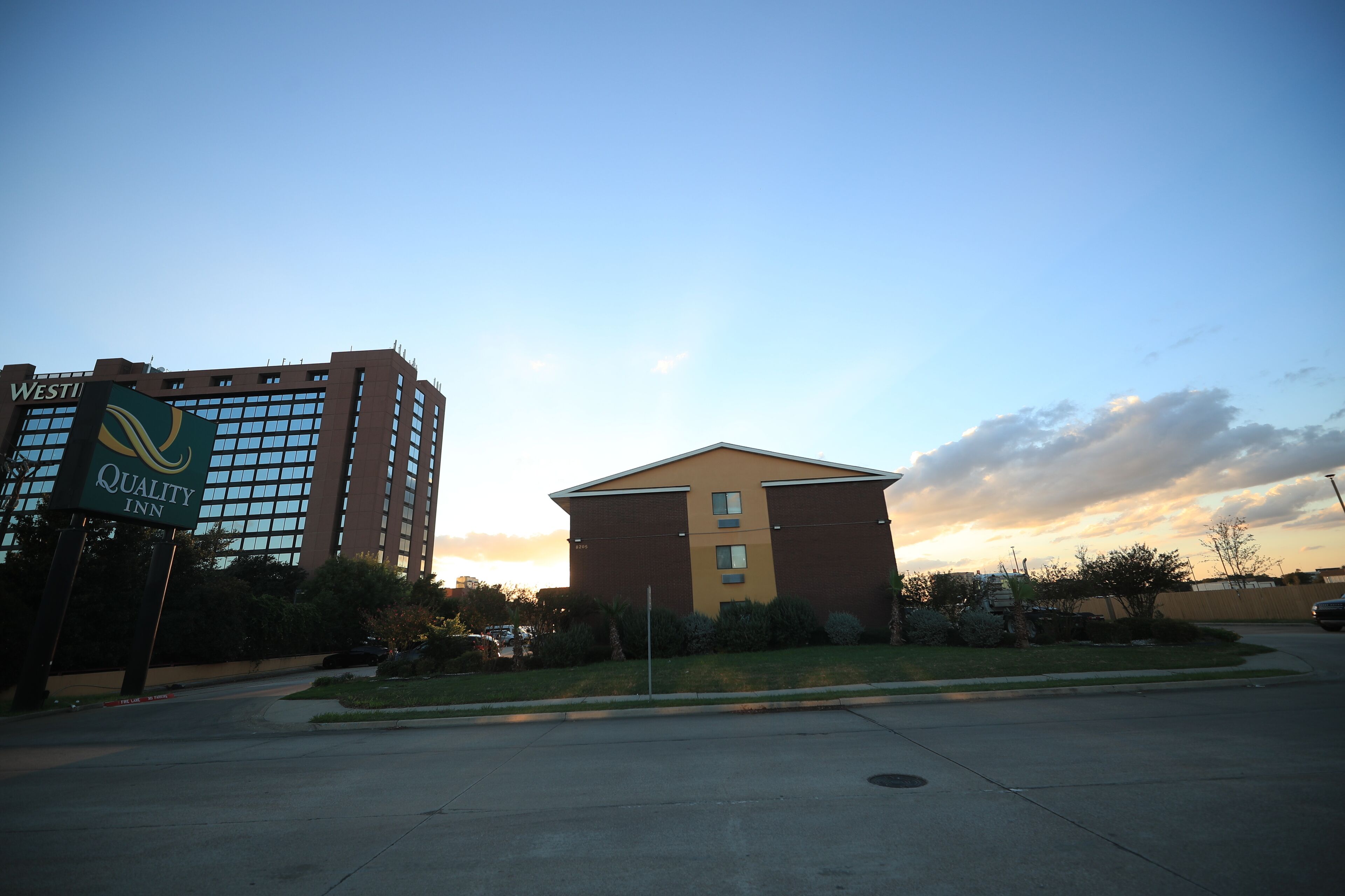 A hotel with a sign for Quality Inn, a parking lot, and a building with a yellow roof.