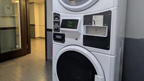 A front view of a modern, compact, white laundry machine with a digital display, a control panel, and a door. - Quality Inn DFW Airport North (Irving)
