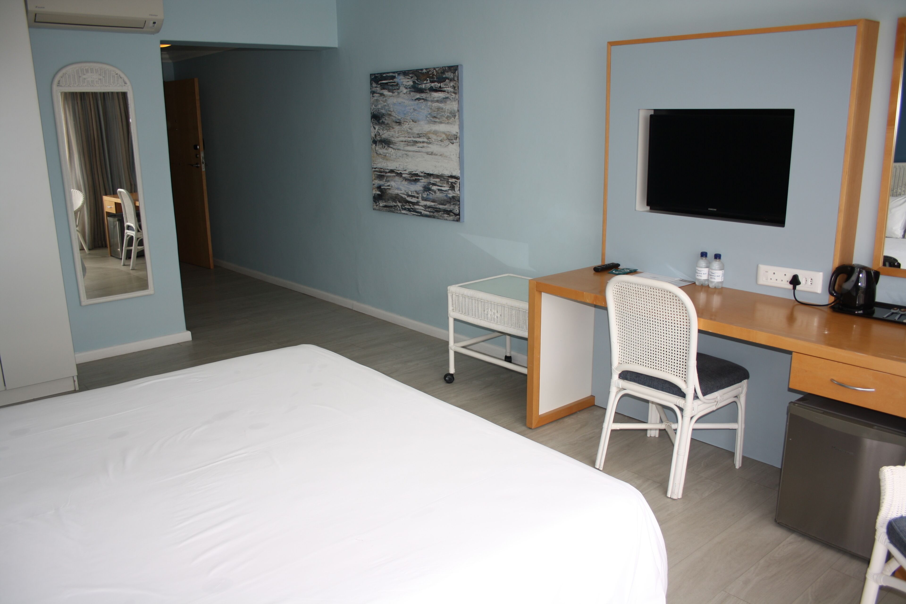 A hotel room with a bed, a desk, a chair, a small refrigerator, a television, and a mirror.