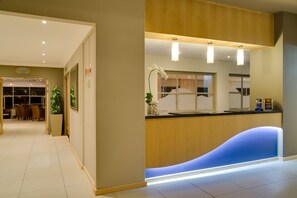 A reception area with a wooden counter, a blue illuminated section, and a sign indicating a bar and lounge.