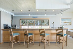 A bar area with wooden chairs and a counter displaying bottles.