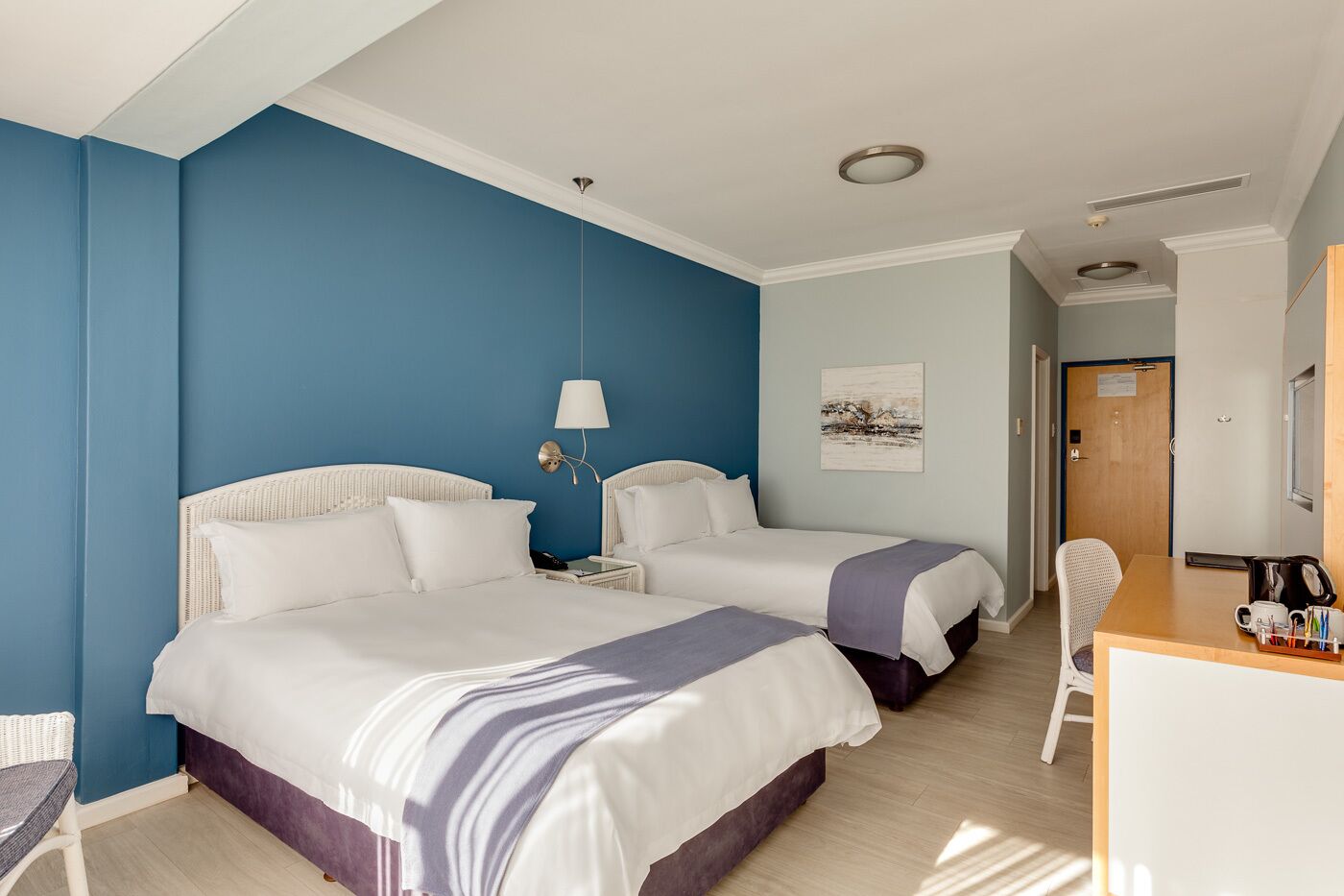 A hotel room with two beds, a desk, a chair, and a painting on the wall.