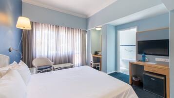 Habitación de hotel con una cama grande, un escritorio con silla, un televisor y un refrigerador pequeño.
