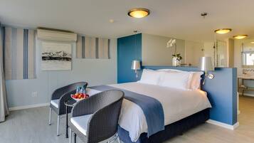 Ein Hotelzimmer mit einem Bett, zwei Stühlen, einem kleinen Tisch mit Früchten und Wasserflaschen, einem Spiegel und einem durch eine offene Tür einsehbaren Badezimmer.