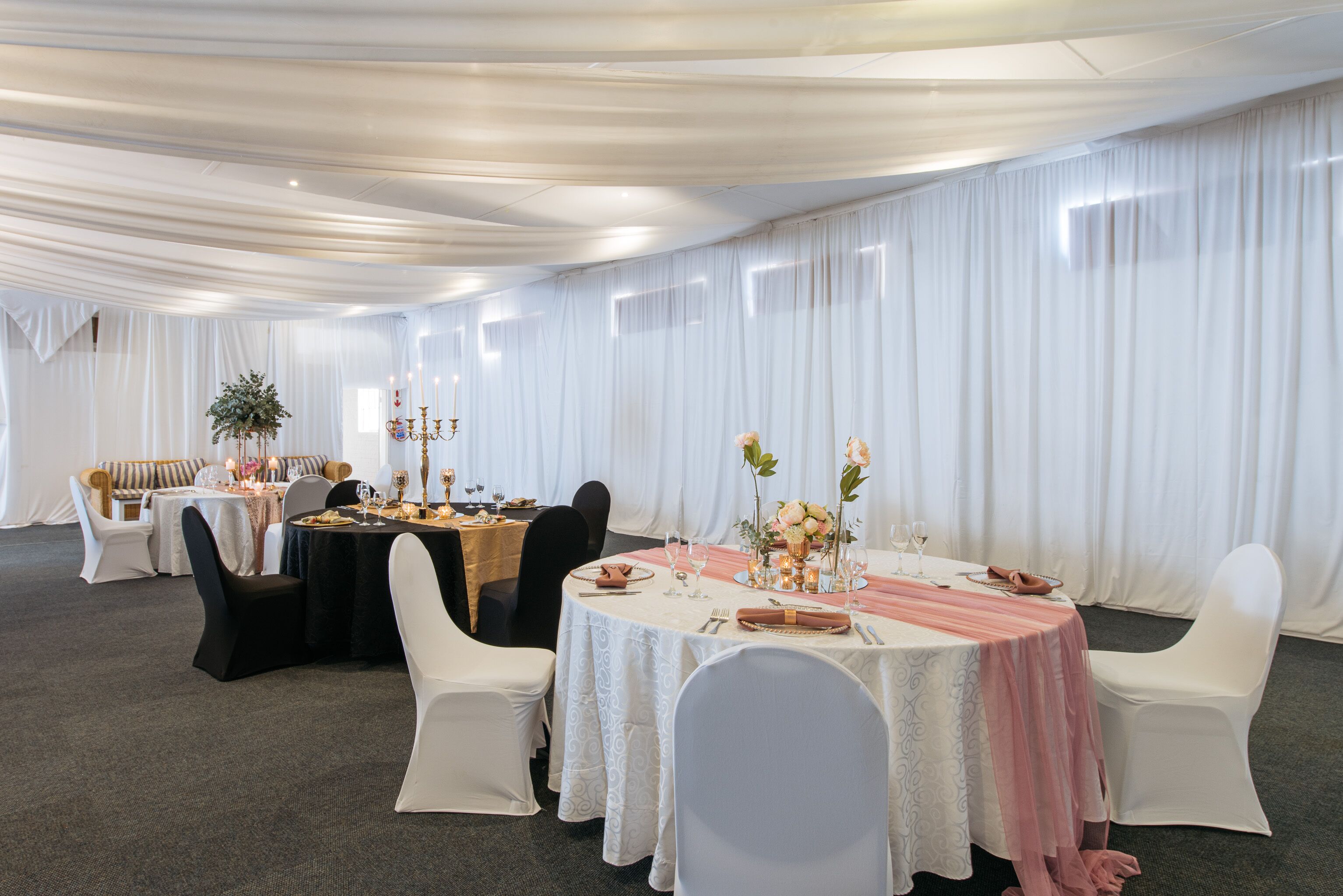 Een balzaal met ronde tafels, witte stoelen en gordijnen.