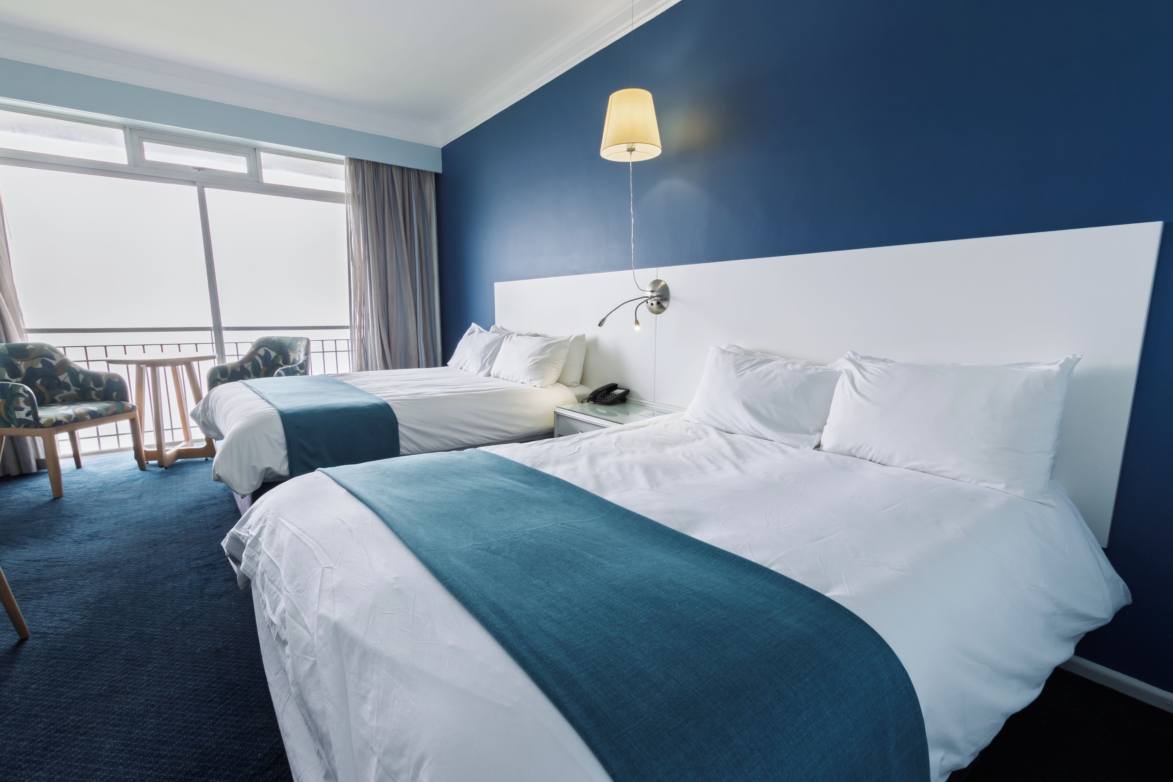 A hotel room with two beds, a balcony, and a view of the sky.