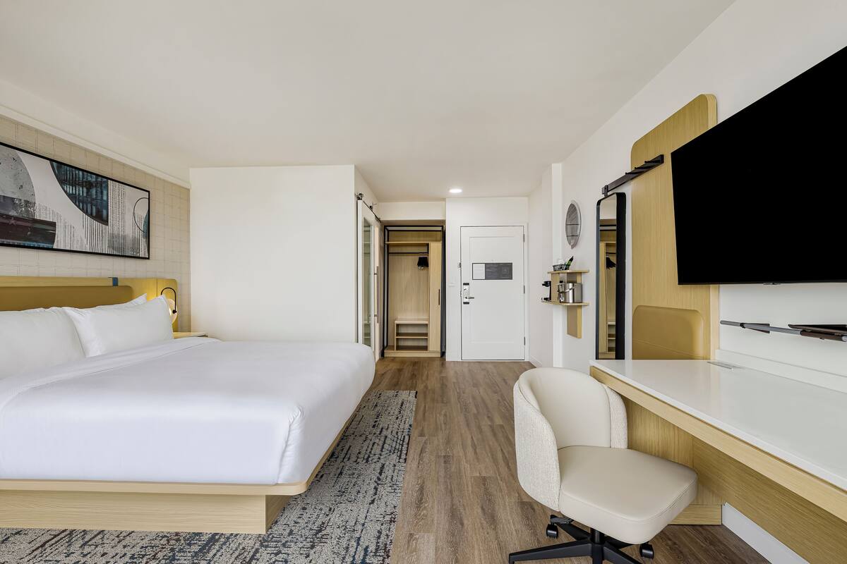 A hotel room with a bed, desk, chair, TV, and a door leading to a bathroom.
