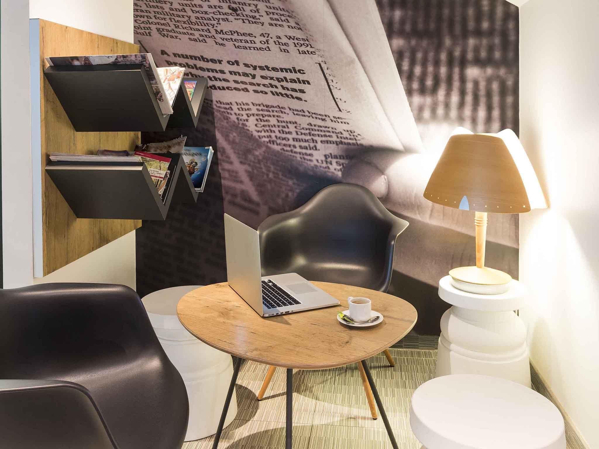 A modern room with a laptop on a round table, a chair, a lamp, and a bookshelf.