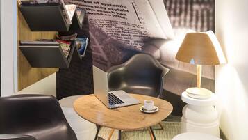 A modern room with a laptop on a round table, a chair, a lamp, and a bookshelf.