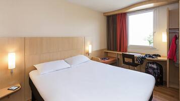 Une chambre d’hôtel équipée d’un lit, d’un bureau, d’une chaise, d’une armoire et d’une fenêtre avec des rideaux.