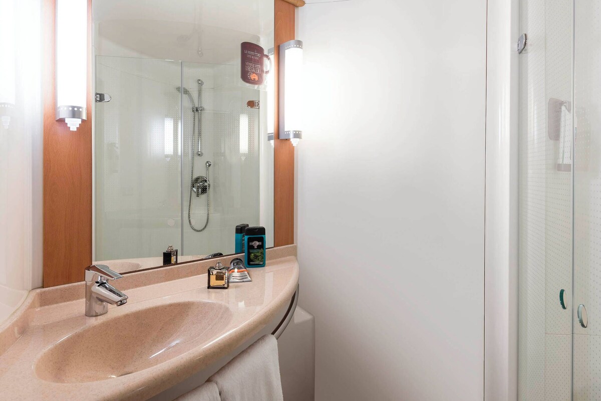 Un baño con un lavabo color beige, un espejo, cabina de ducha de vidrio y una toalla colgada en la pared.