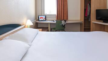 A hotel room with a bed, a desk with a laptop, a chair, a television, and a wardrobe.