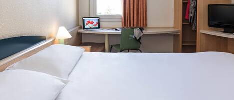 A hotel room with a bed, a desk with a laptop, a chair, a television, and a wardrobe.