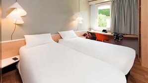 A hotel room with two beds, a desk, a chair, a window with curtains, and a lamp. - ibis Montbeliard (Montbeliard)