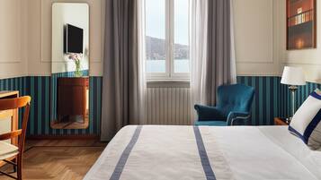 Ein Hotelzimmer mit Bett, Stuhl, Schreibtisch, Spiegel, einem Fenster mit Vorhängen und einem Bild an der Wand.