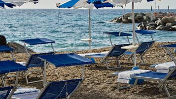 Na praia, areia preta, espreguiçadeiras, guarda-sóis