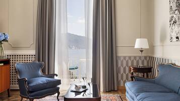 Ein Zimmer mit Meerblick, ausgestattet mit zwei blauen Sesseln, einem kleinen Tisch mit Schale und Weingläsern sowie einer Lampe auf einem Beistelltisch.