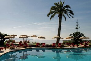 A pool area with lounge chairs and umbrellas, a palm tree, and a view of the sea. - Grand Hotel Miramare (Santa Margherita Ligure)