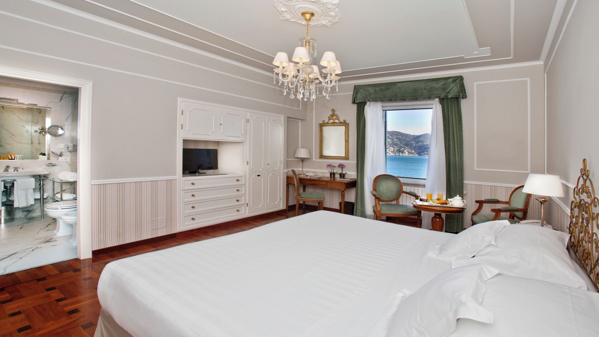 Habitación de hotel con una cama grande, un escritorio con silla, una tocador con espejo y vista al mar.