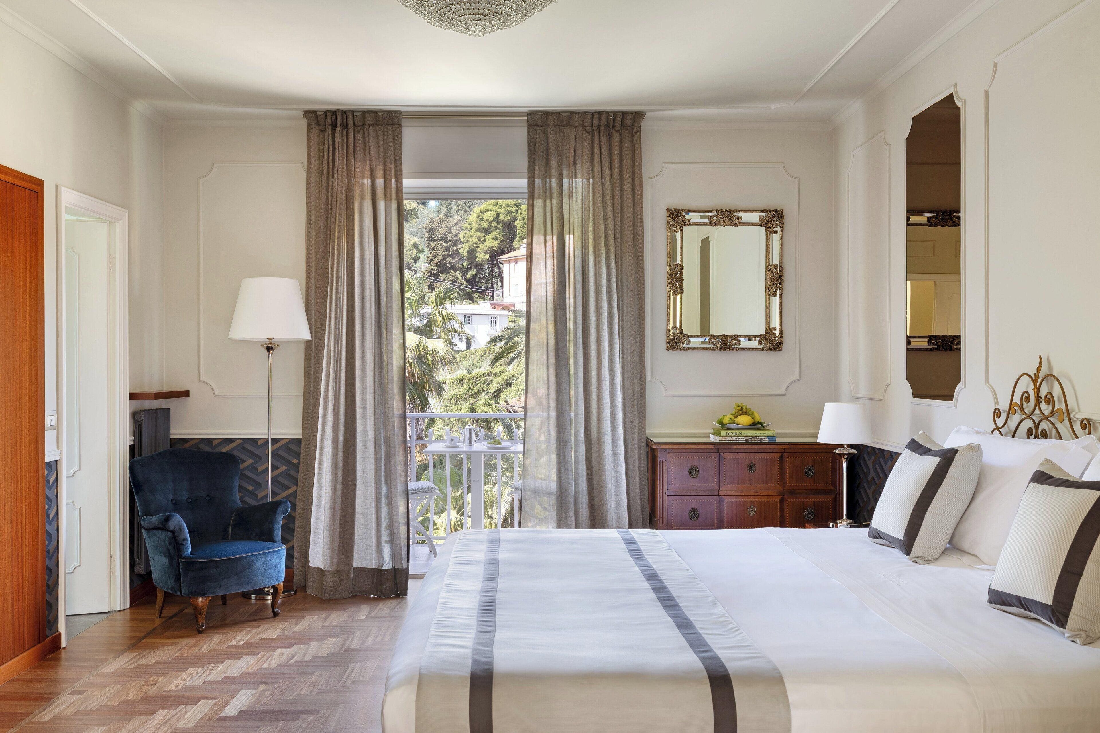 Camera d'albergo con un letto grande, una poltrona, una cassettiera e uno specchio.