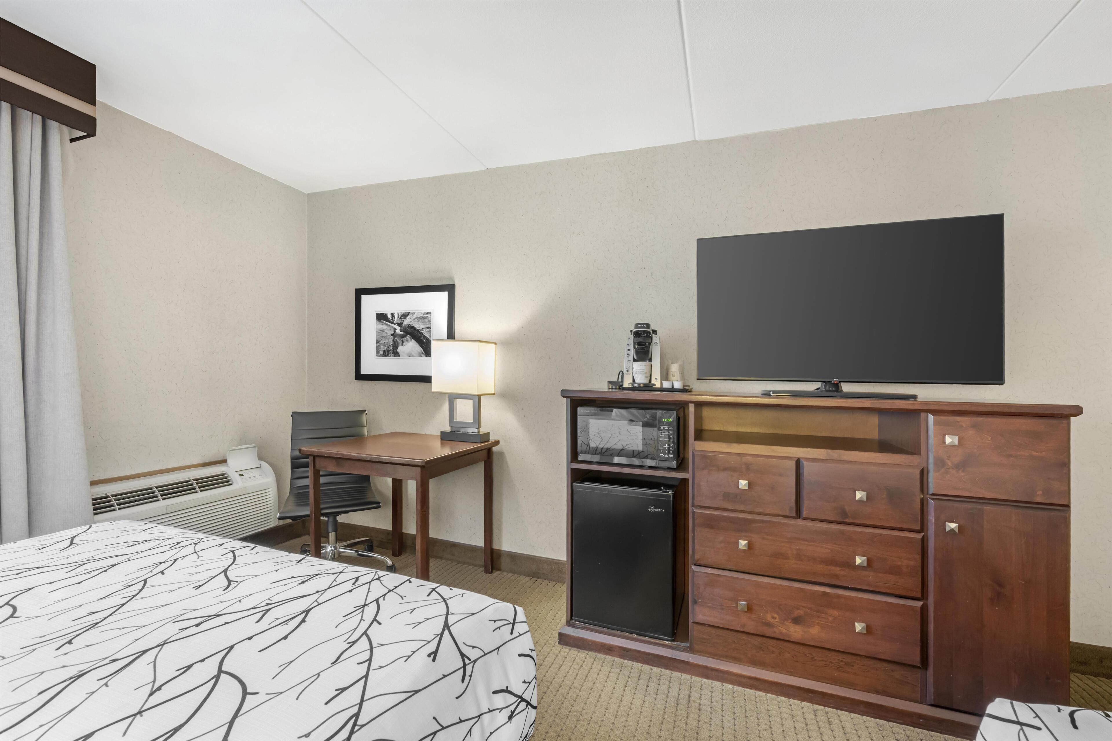Una habitación de hotel con cama, escritorio, televisor, microondas y cómoda.