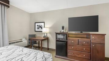 Una habitación de hotel con cama, escritorio, televisor, microondas y cómoda.