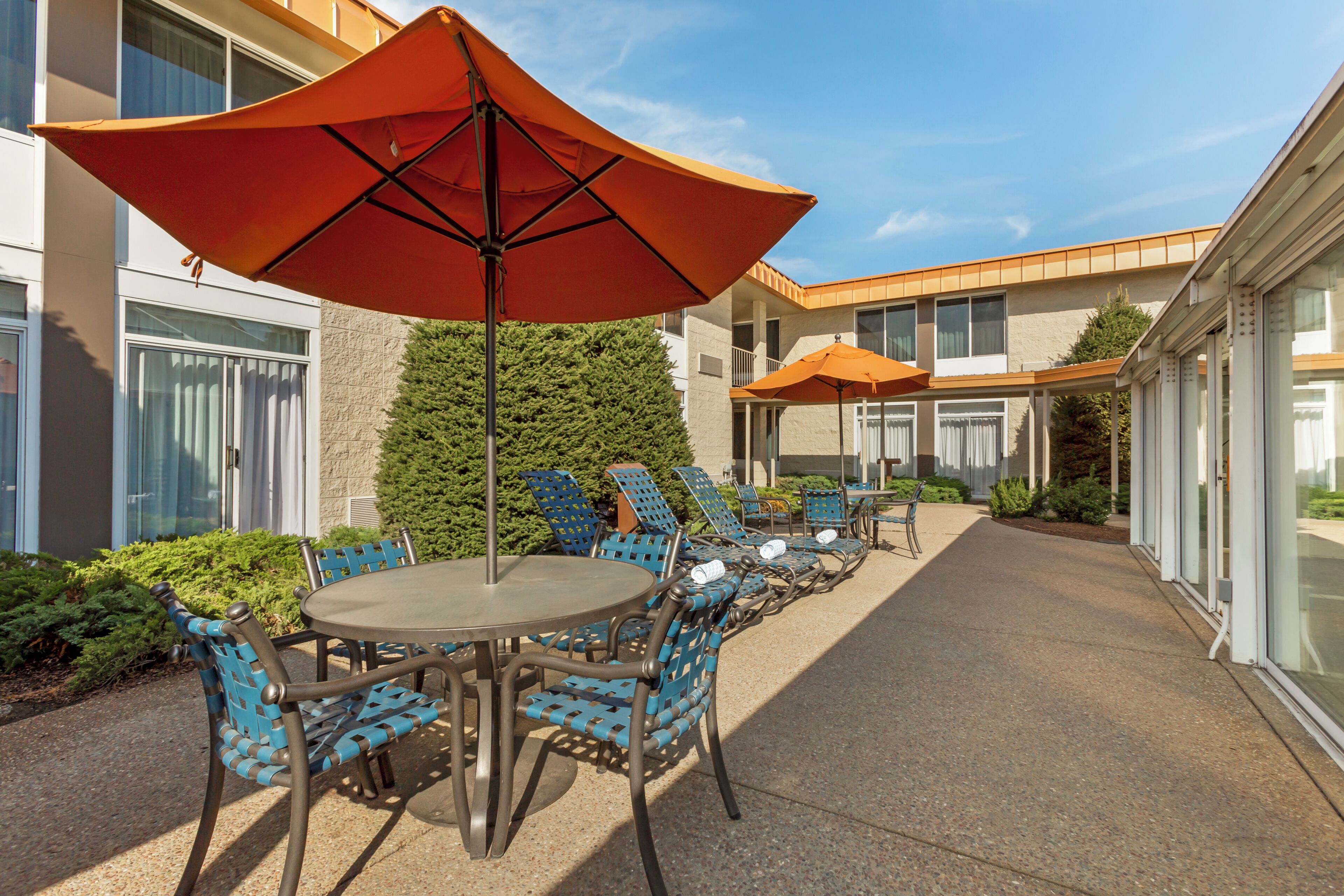 An outdoor seating area with round tables and chairs, large umbrellas, and a hedge.