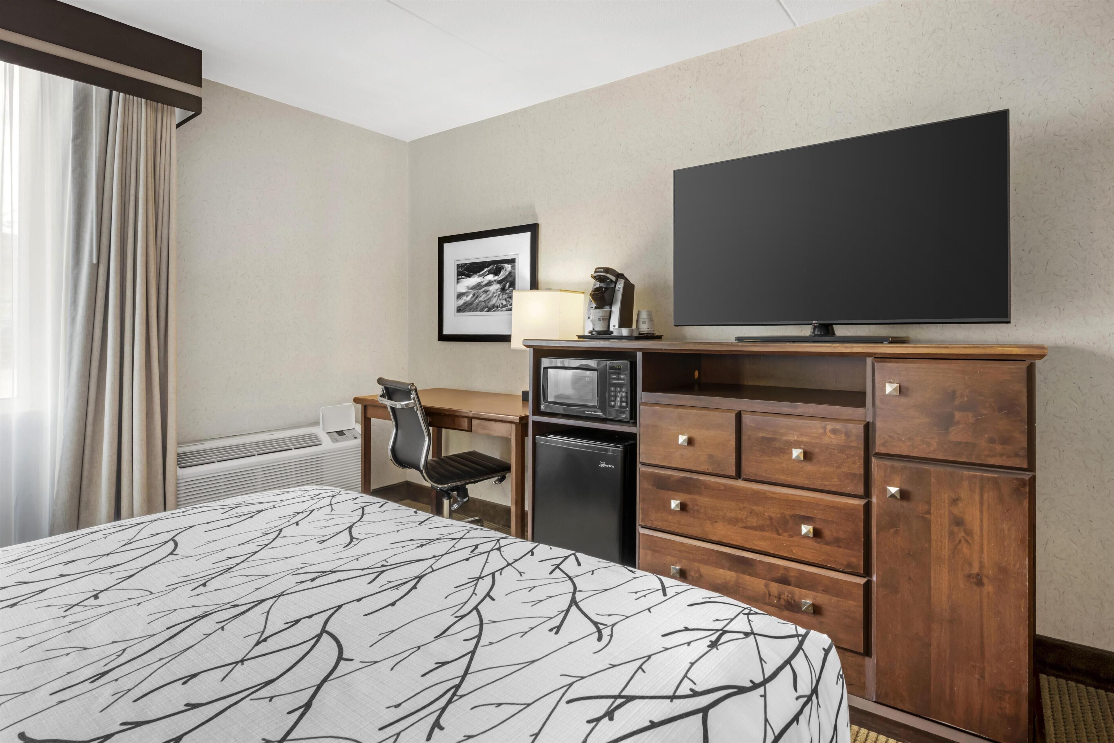 Hotelkamer met een bed, een bureau met stoel, een televisie, een magnetron en een koelkast.