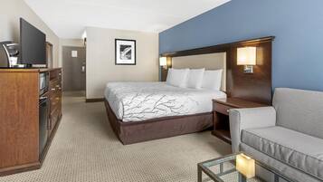 A hotel room with a bed, a sofa, a desk with a flat-screen TV, and a coffee machine.