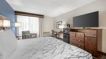 Habitación de hotel con una cama grande, un escritorio con silla, televisión, armario y ventana con cortinas.