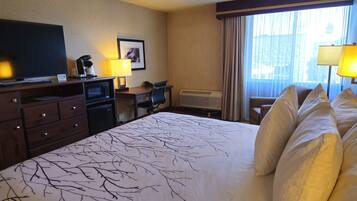 A hotel room with a large bed, a desk with a chair, a television, a microwave, and a window with curtains.