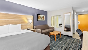 Habitación de hotel con cama, sofá, una mesita, espejo y puerta.