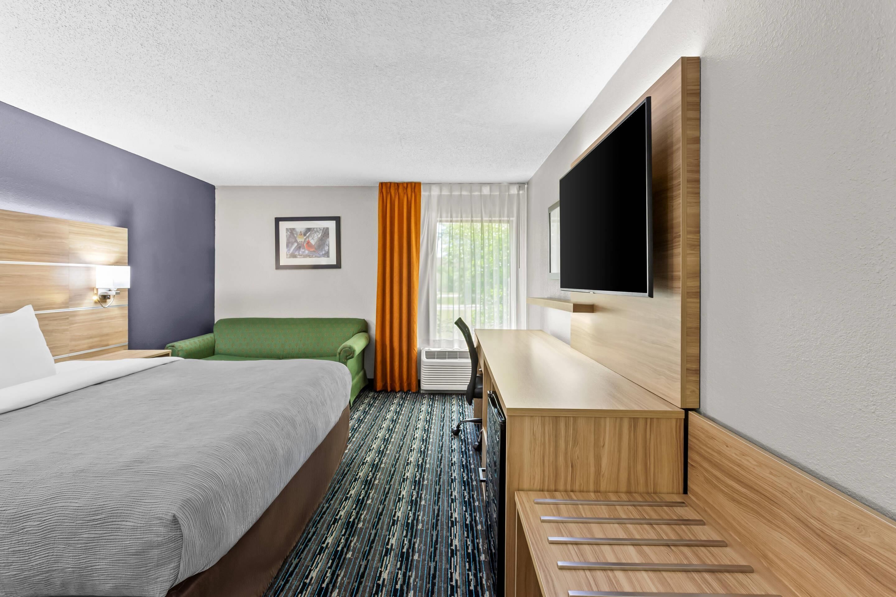Habitación de hotel con cama, escritorio, silla, televisión y ventana con cortinas.