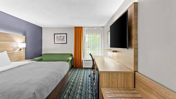 Habitación de hotel con cama, escritorio, silla, televisión y ventana con cortinas.