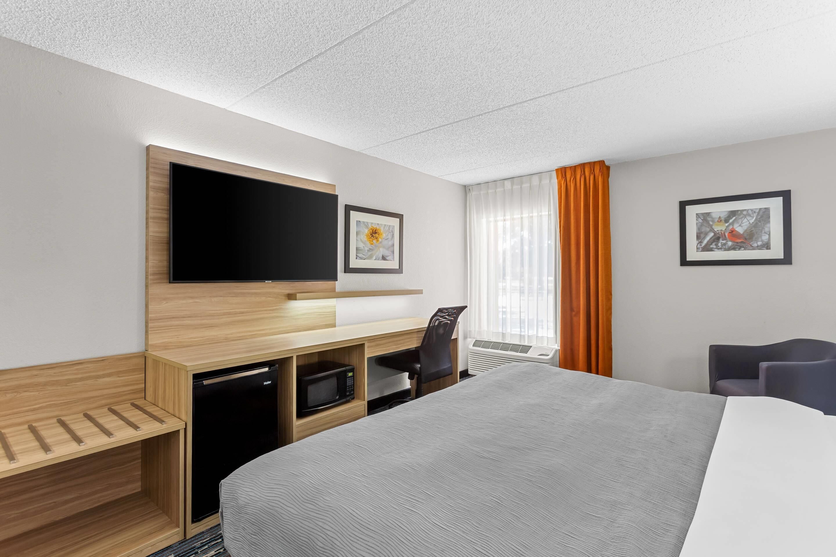 Een hotelkamer met een bed, een televisie, een bureau met een magnetron, een stoel en twee ingelijste foto's aan de muur.