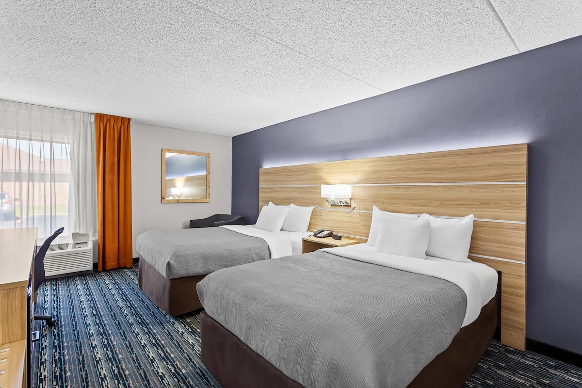Ett hotellrum med två sängar, ett skrivbord, en stol, en spegel och ett fönster med gardiner.