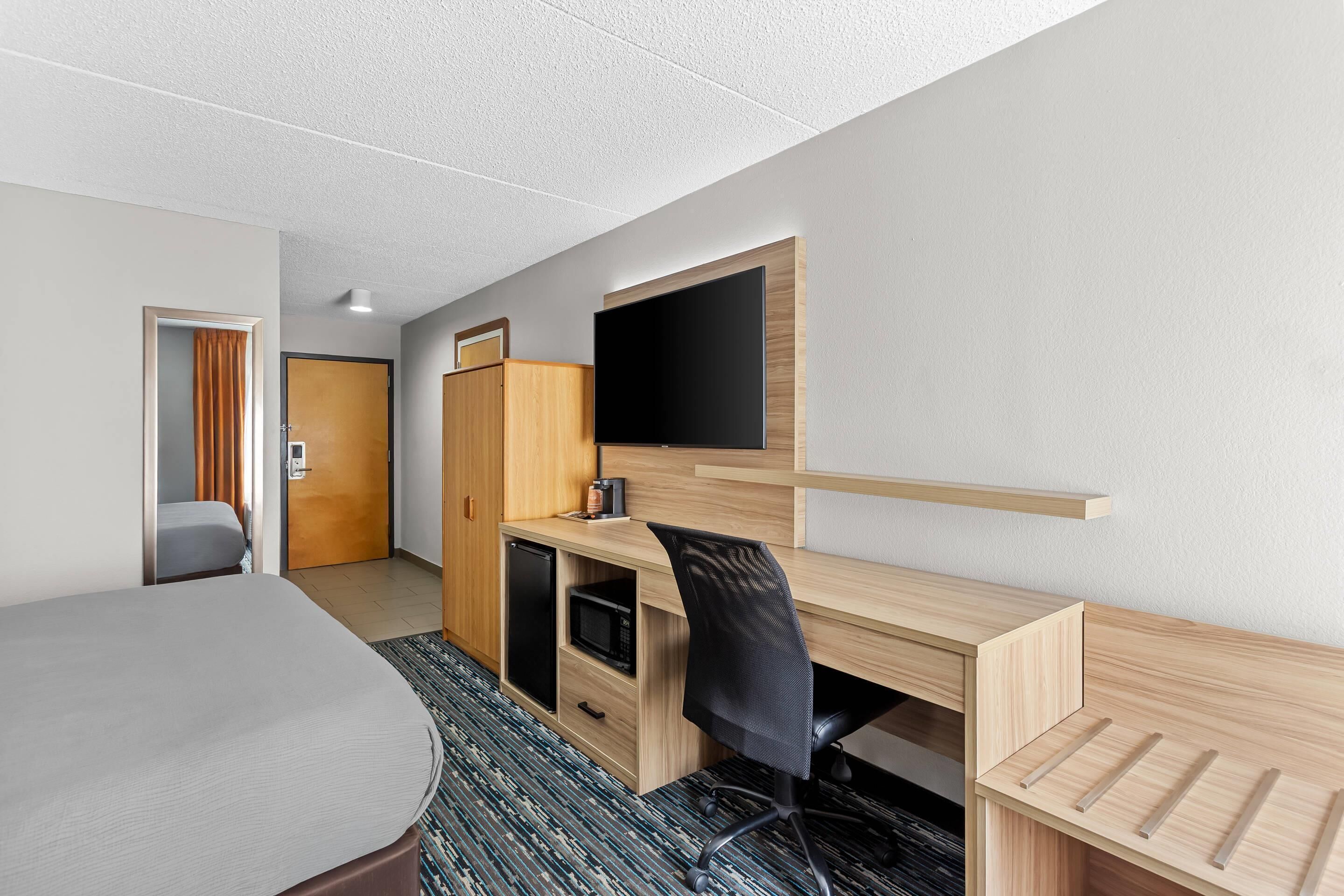 A hotel room with a bed, a desk with a flat-screen TV, a microwave, and a wardrobe.