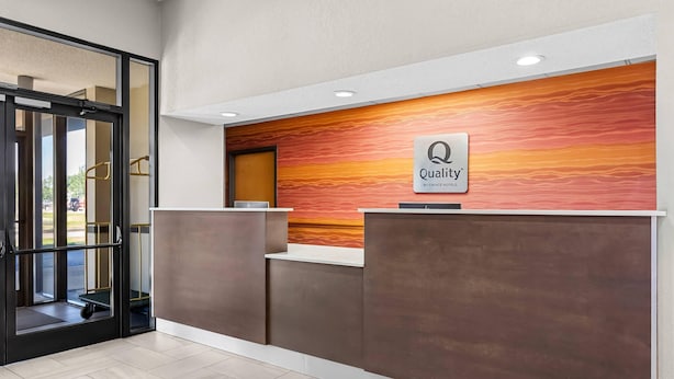 Un área de recepción con diseño moderno, un mostrador de recepción y un cartel que dice 'Quality by Choice Hotels'.