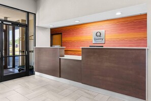 Un área de recepción con diseño moderno, un mostrador de recepción y un cartel que dice 'Quality by Choice Hotels'.