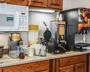 A kitchen area with a microwave, waffle maker, coffee machine, and syrup dispenser.