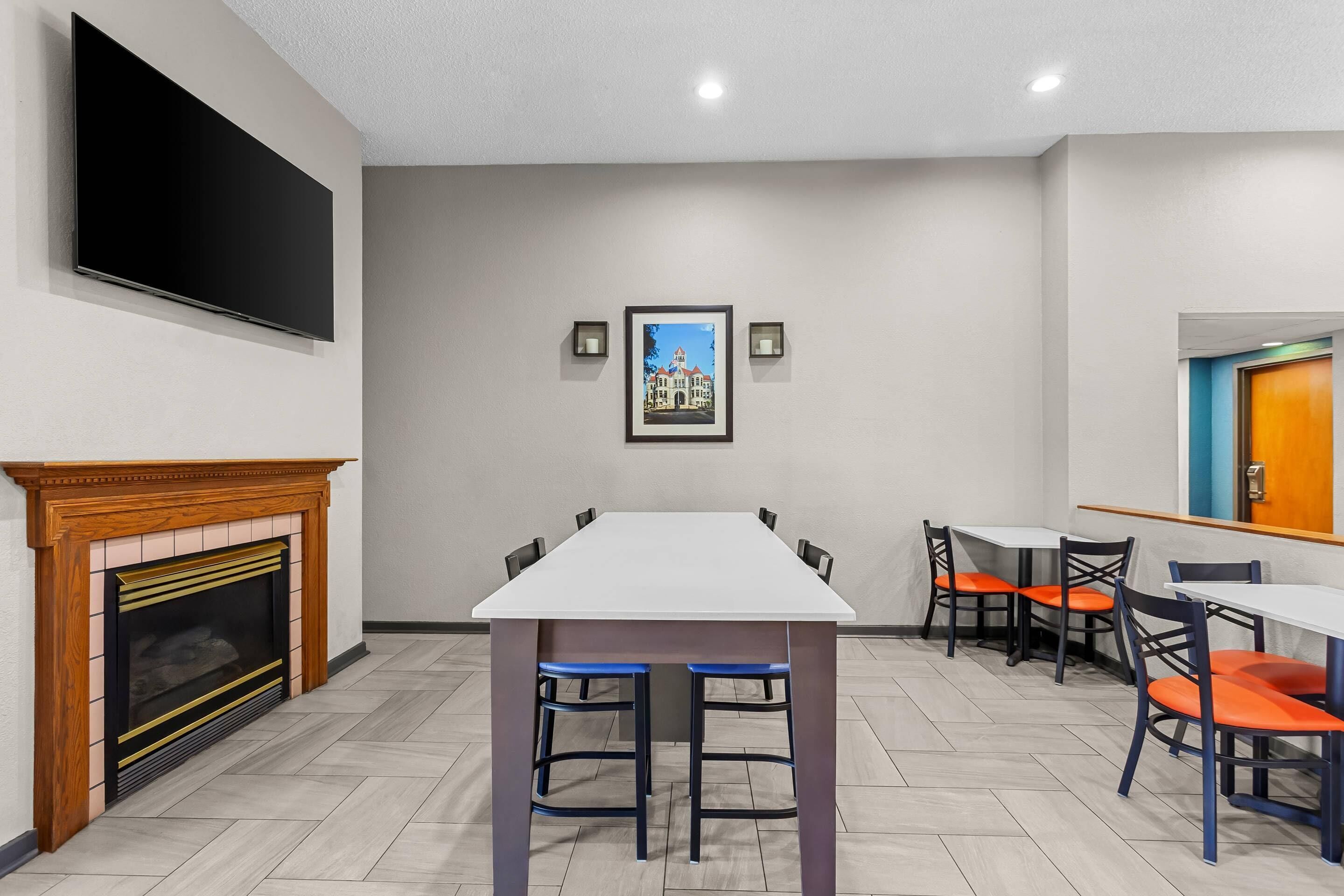 A hotel room with a fireplace, a large flat-screen TV, a dining table with chairs, and a framed picture on the wall.