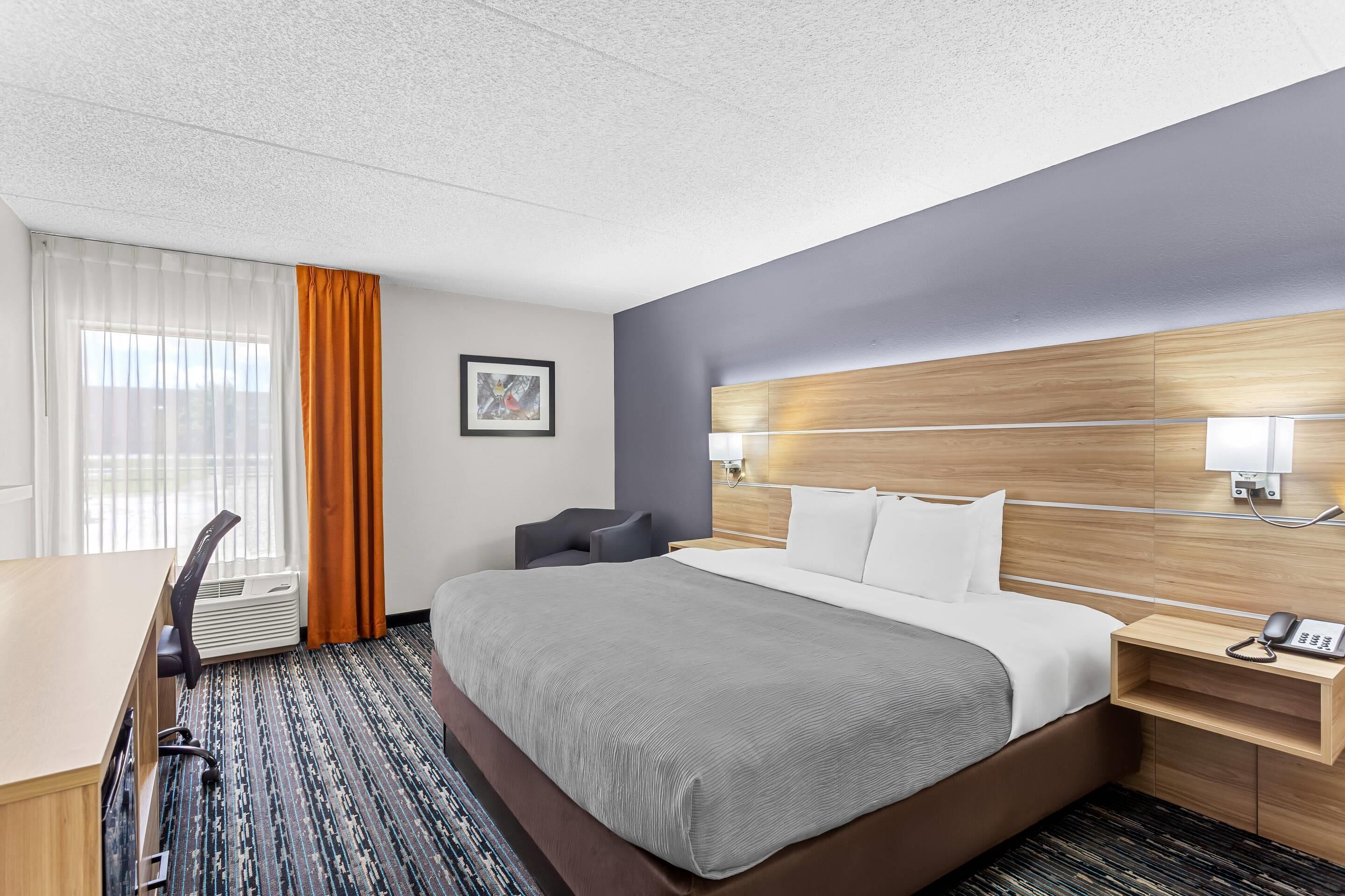 A hotel room with a bed, desk, chair, and a picture on the wall.