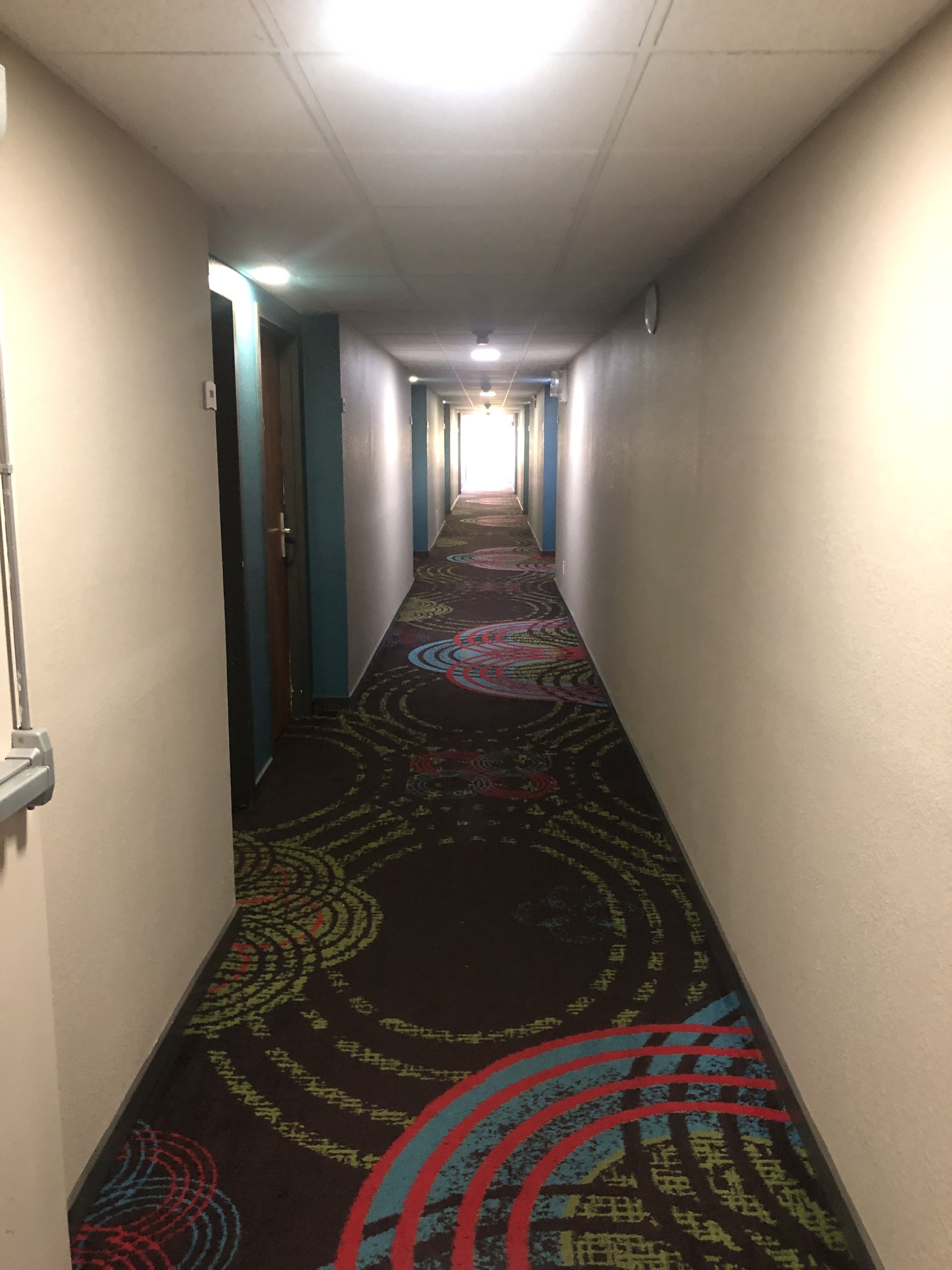 A hallway with a patterned carpet, white walls, and a door at the end.