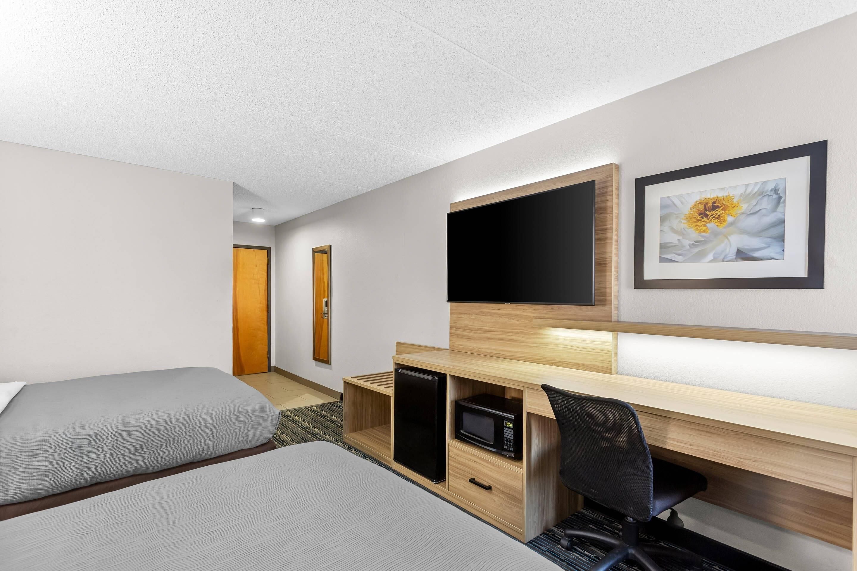 Ein Hotelzimmer mit zwei Betten, einem Schreibtisch mit Computer, einem Fernseher und einer Mikrowelle.