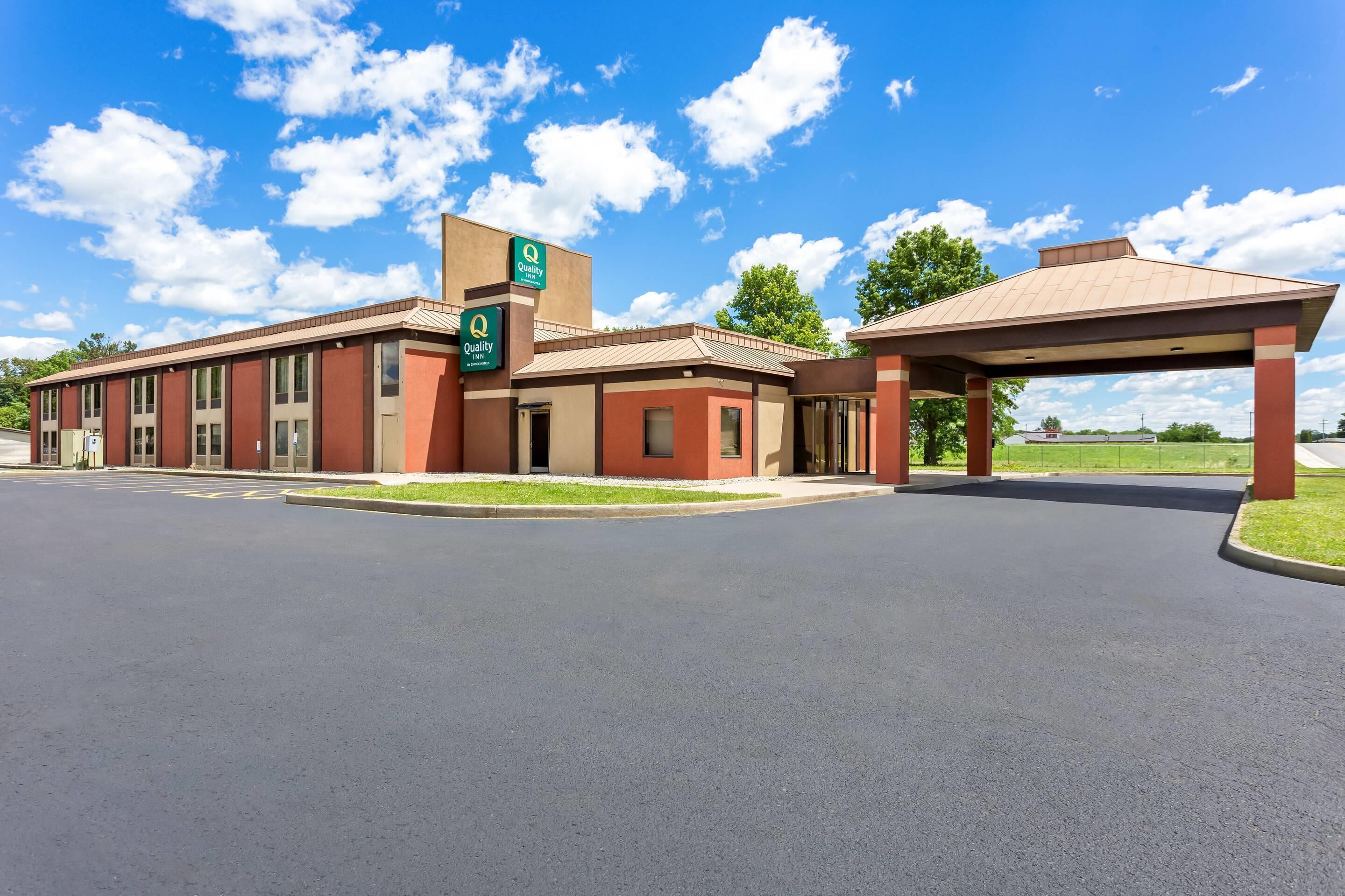 A hotel with a parking lot, a covered waiting area, and a sign indicating 'Quality' services.